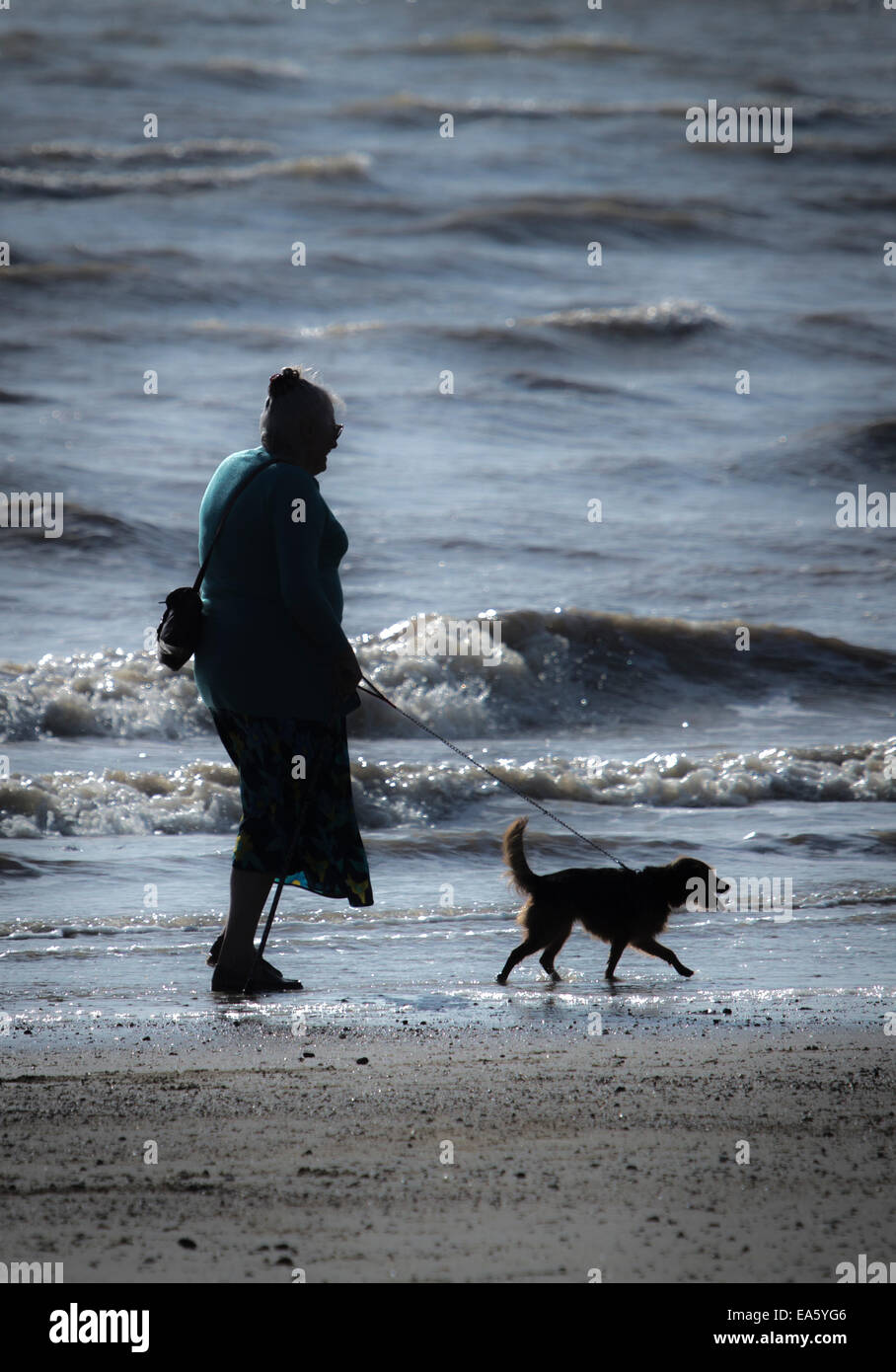 Eine Silhouette von eine ältere Dame zu ihrem Hund am Strand entlang in Littlehampton, West Sussex. Stockfoto