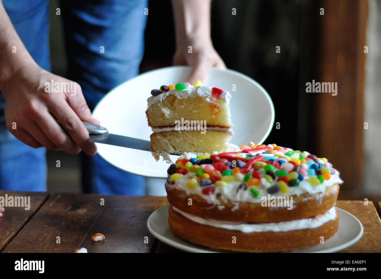 Man schneidet ein Stück Geburtstagstorte Stockfoto