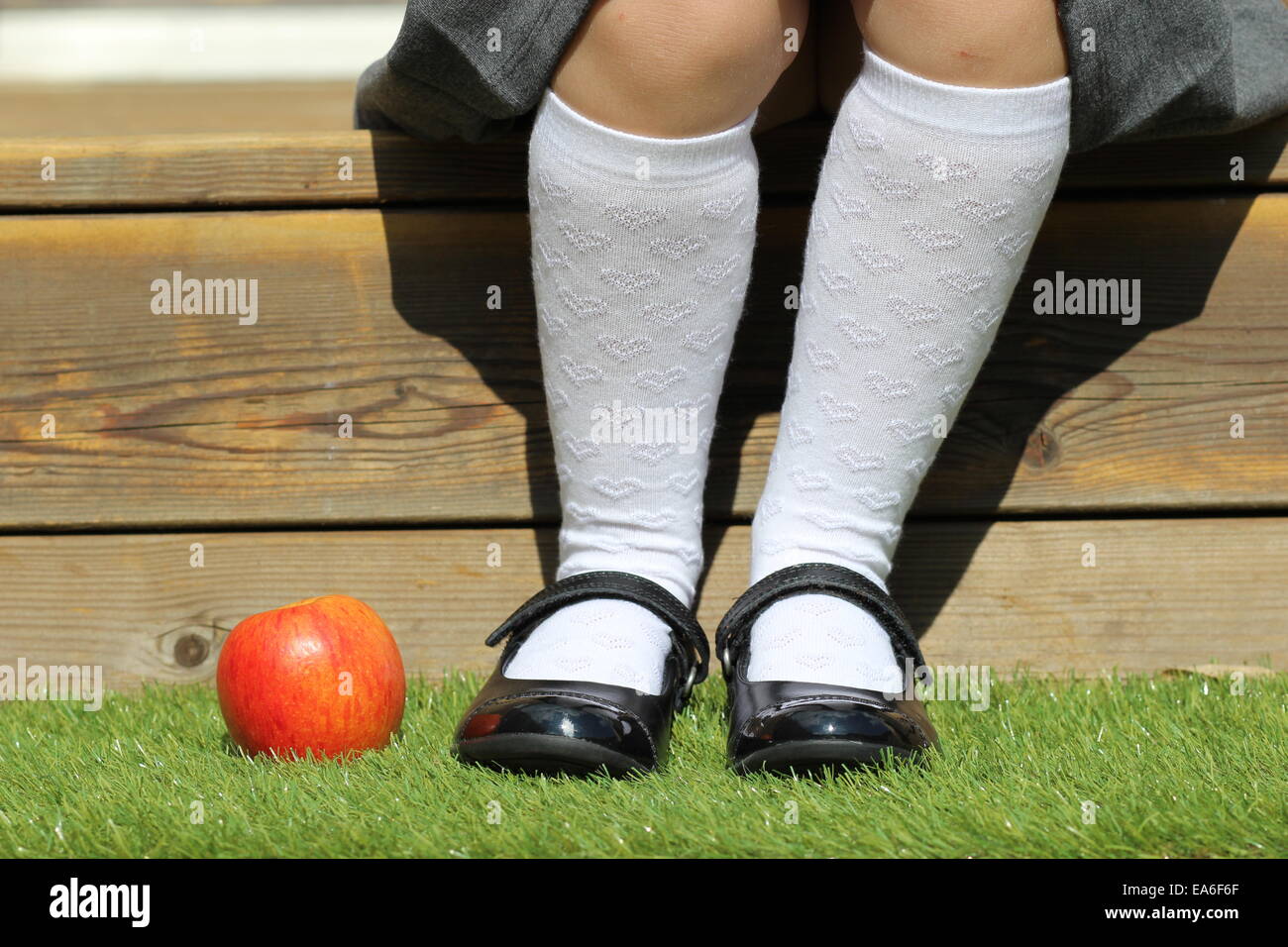 Mädchen sitzen auf Schritt mit Apple auf Rasen durch ihre Füße Stockfoto