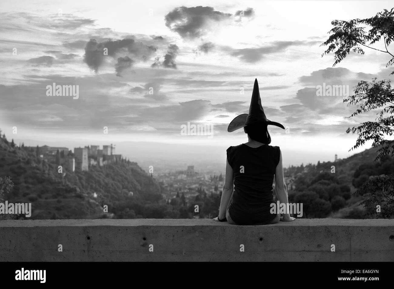 Silhouette einer Frau sitzt auf einer Mauer mit Hexen Hut Stockfoto