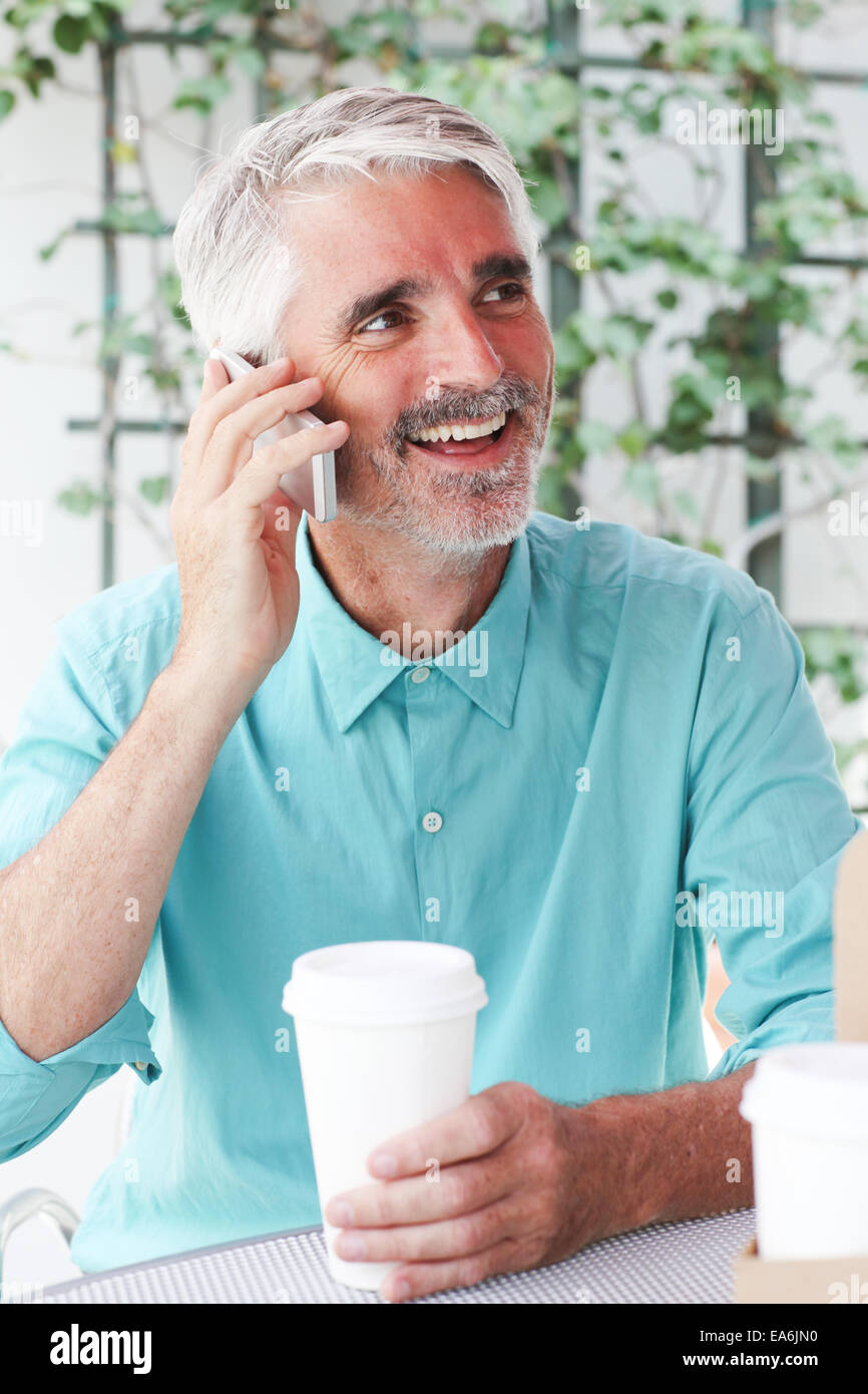 Geschäftsmann mit Kaffeetasse in der hand telefonieren im Straßencafé Stockfoto