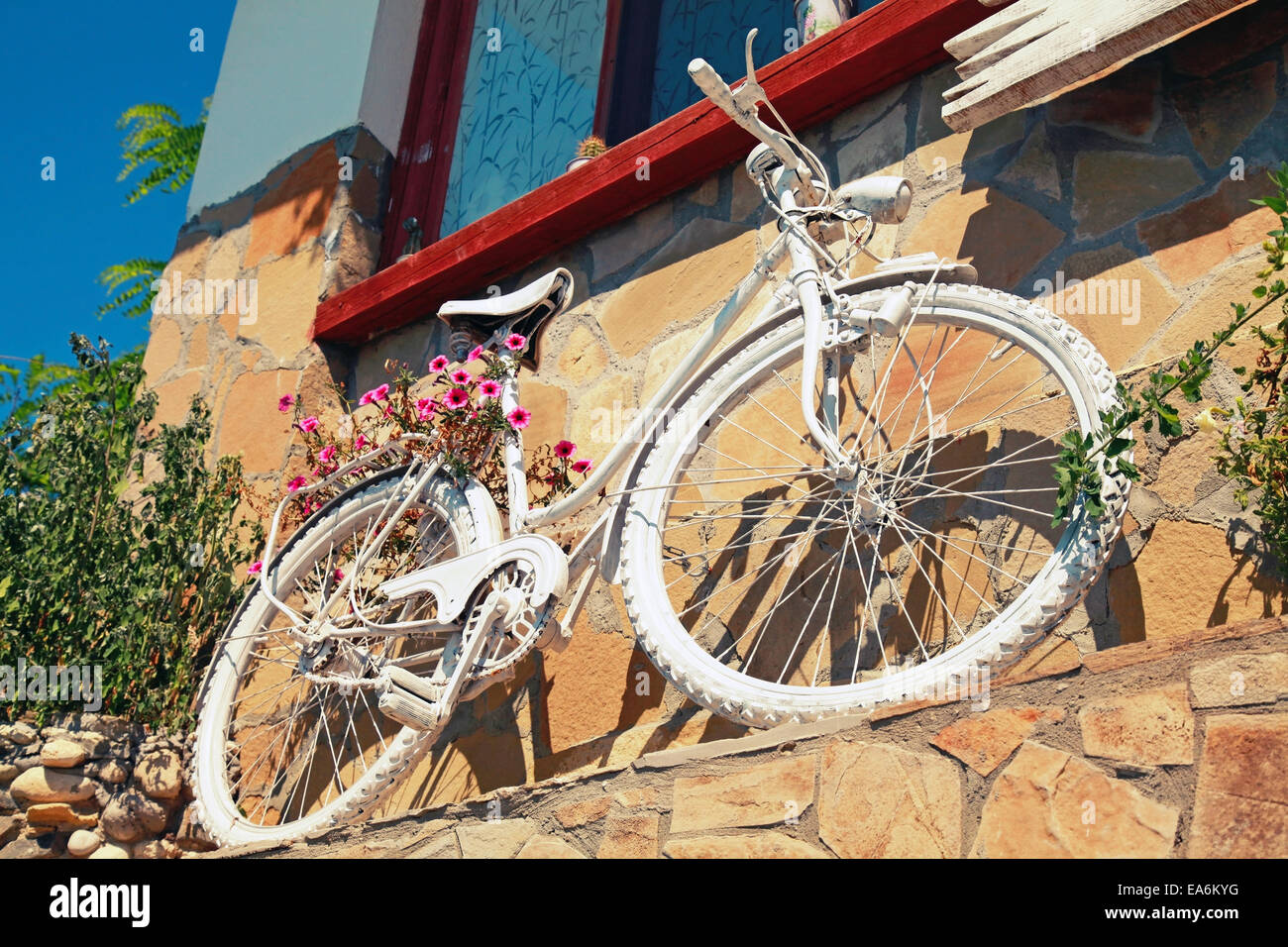 Weiße Vintage Fahrrad mit roten Blüten steht in der Nähe von alten Steinmauer Stockfoto