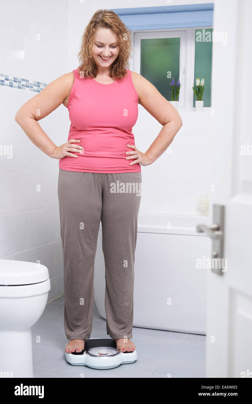 Glückliche Frau wiegen sich auf die Waage im Badezimmer Stockfoto