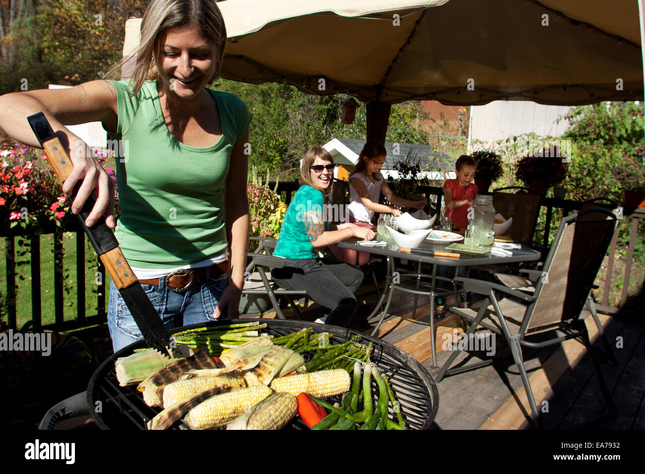 Mutter stand Barbecue-Grill mit Zange mit Töchtern (8-9) im Hintergrund Stockfoto