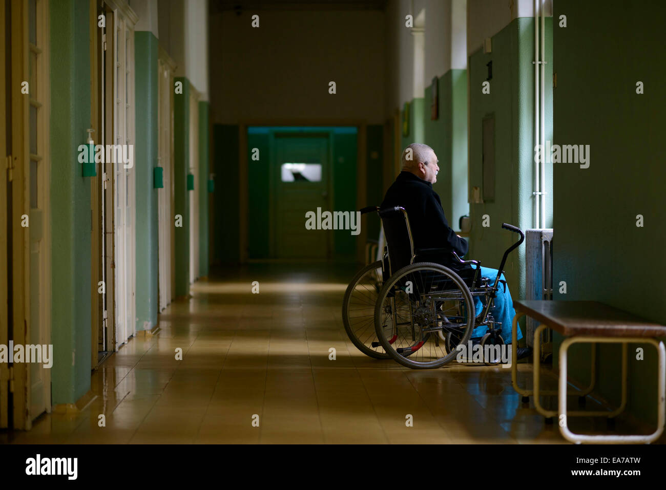 Alter Mann auf einen Rollstuhl Blick aus einem Fenster allein auf einen langen Korridor Stockfoto