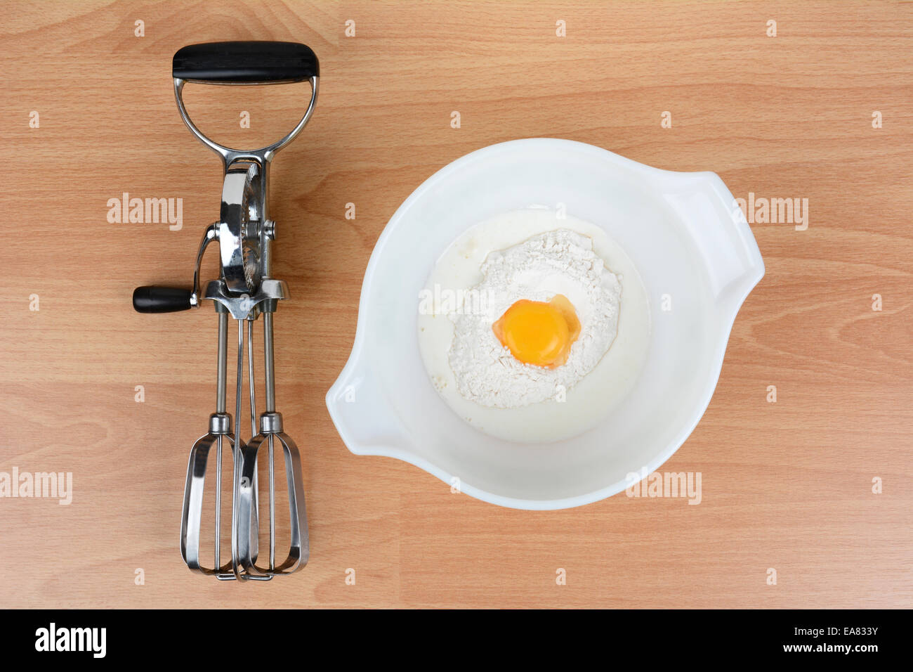 Hohen Winkel Schuss aus einer Schüssel mit Milch, Ei und Mehl mit einem alten altmodischen Handmixer auf dem Tisch daneben. Querformat. Stockfoto