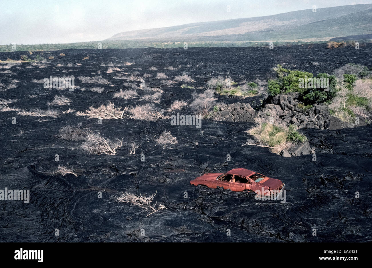 Ein altes rostiges Auto bleibt entlang einer Straße bedeckt von Lava aus einem Vulkanausbruch in the1980s auf der Big Island von Hawaii, USA. Stockfoto