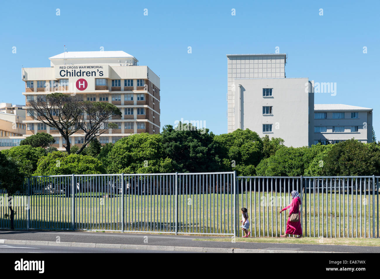 Mutter und Kind zu Fuß entlang des Zauns zu Red Cross War Memorial Children Hospital, Kapstadt, Südafrika Stockfoto