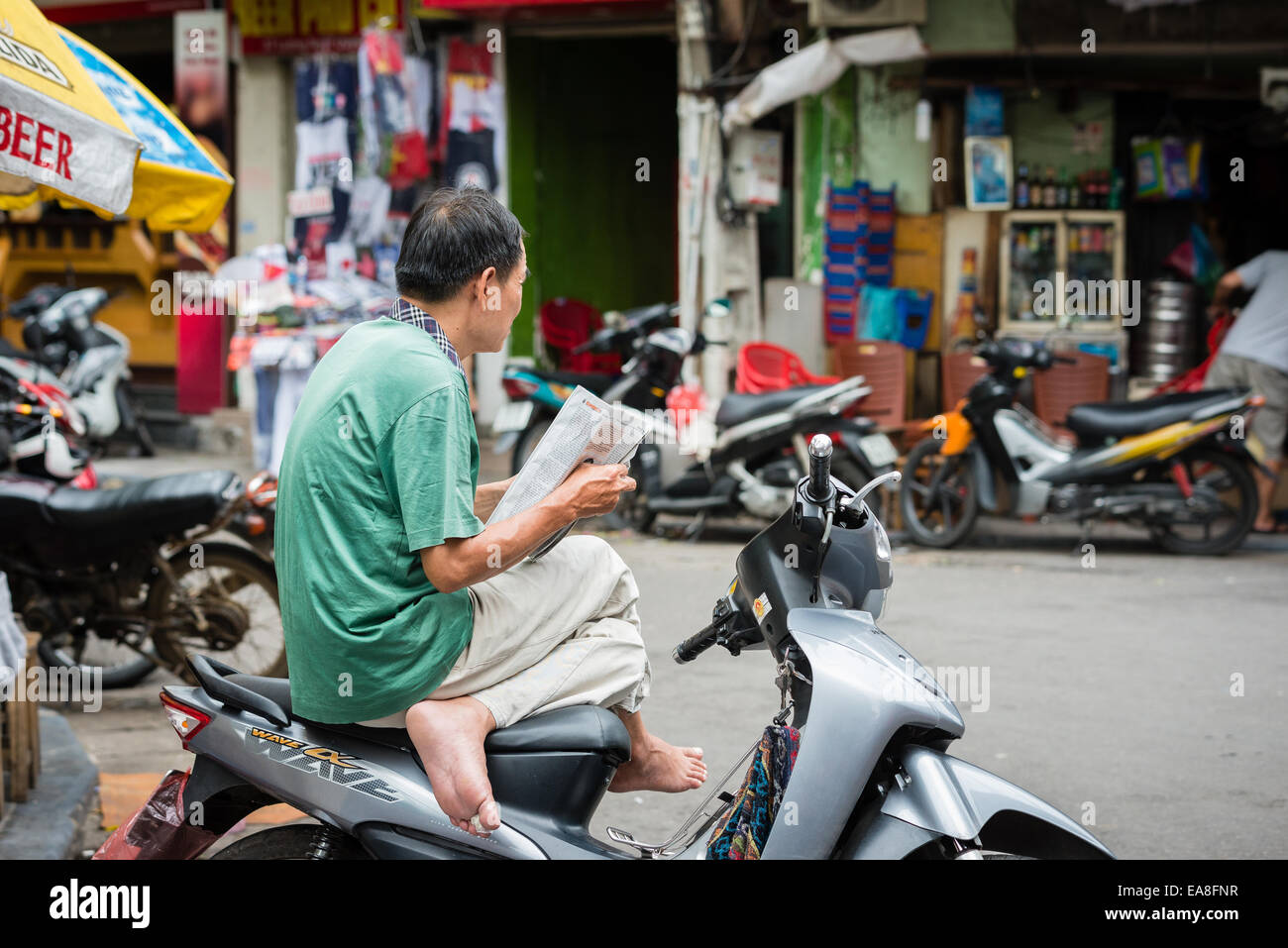 Vietnamesische motor Taxifahrer sitzen auf Fahrrad, Zeitung lesen, während des Wartens auf einen Tarif Stockfoto