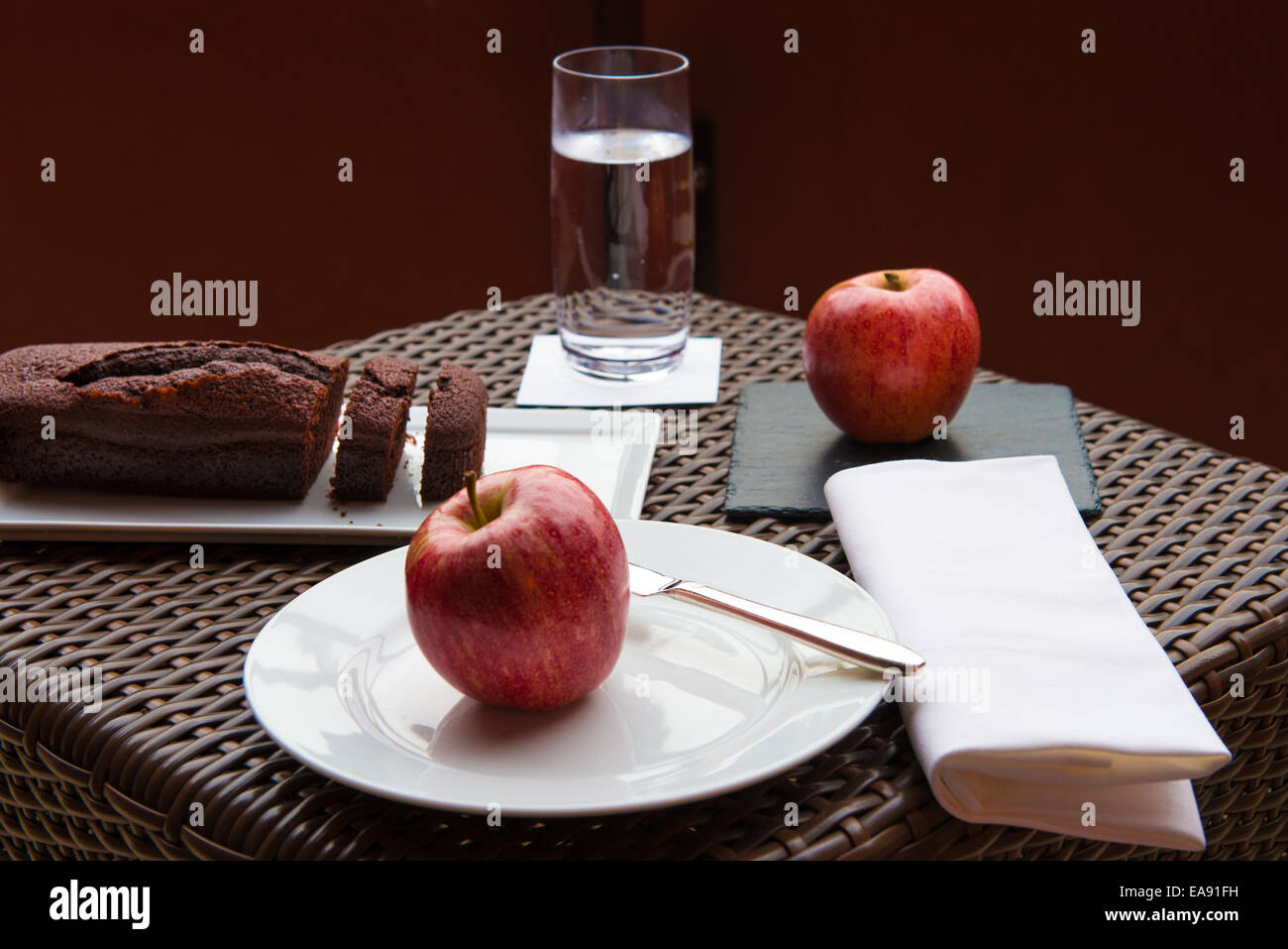 Frühstück auf der Terrasse Wicker Tisch mit Schokoladenkuchen und zwei rote Äpfel Stockfoto