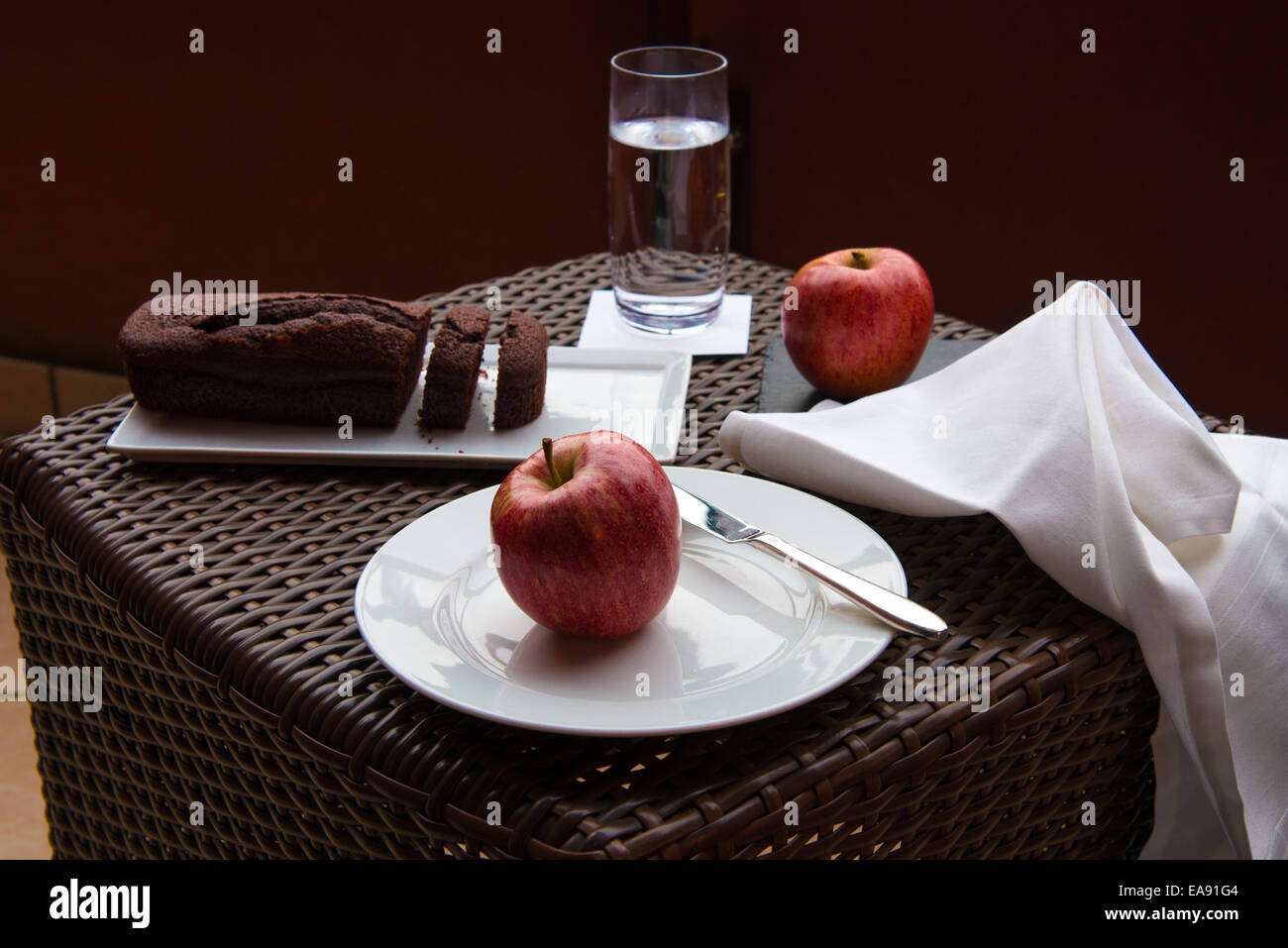 Frühstück auf der Terrasse Wicker Tisch mit Schokoladenkuchen und zwei rote Äpfel Stockfoto