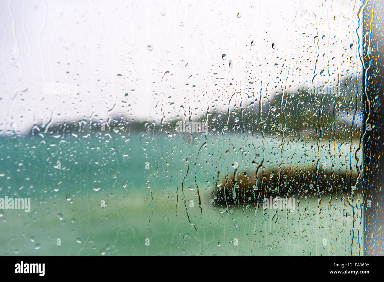Verschwommene Sicht auf den See, gesehen durch ein Fenster mit scharfen Tropfen an einem regnerischen Tag Stockfoto