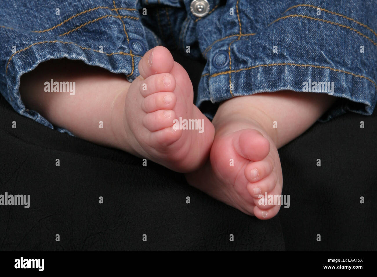 Kleine Füße des Kindes mit Blue Jeans und schwarzem Hintergrund Stockfoto