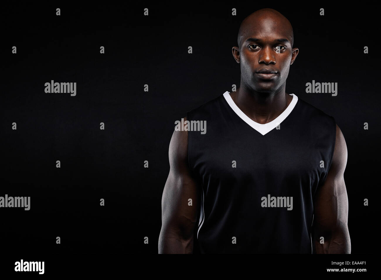 Porträt von muskulösen jungen Mann in Sportbekleidung Blick in die Kamera vor schwarzem Hintergrund. Starken afrikanischen Sportler mit Exemplar Stockfoto
