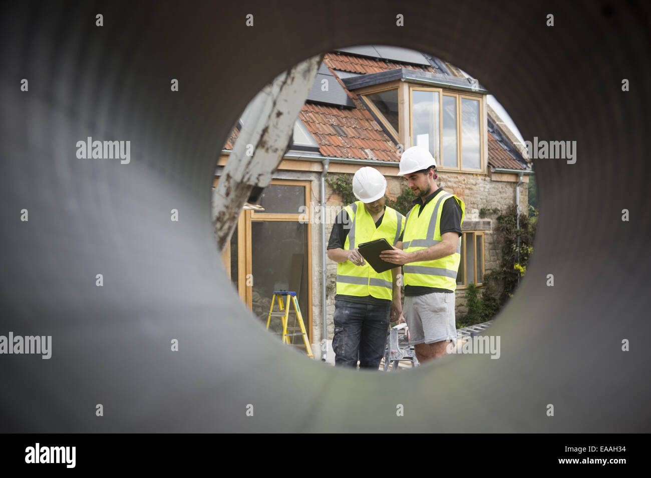 Zwei Bauarbeiter auf einer Baustelle, angezeigt durch ein rundes Rohr. Stockfoto