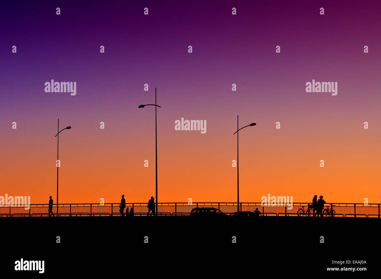 Silhouetten von Menschen über die Brücke im Sonnenuntergang, mit dem Auto oder zu Fuß. Stockfoto