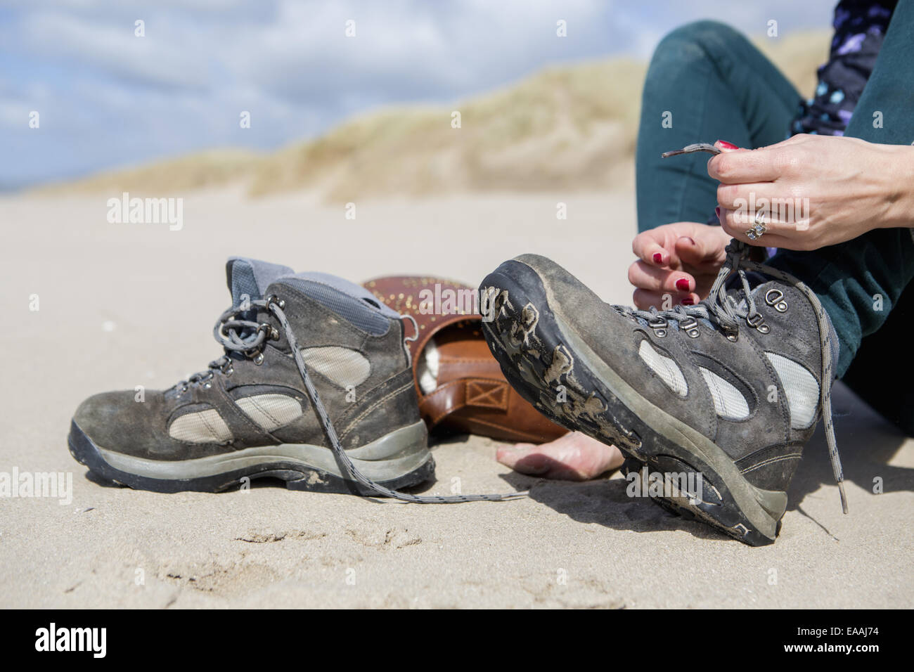 Junge Frau ihre Wanderschuhe ausziehen, am Strand von Harlech. Stockfoto