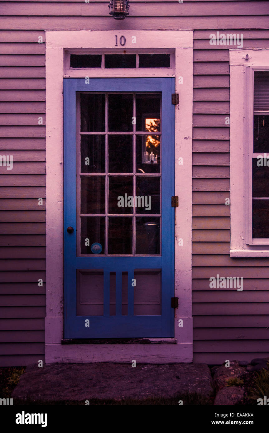 Blauer Sturm Holztür auf alten, rustikalen Maine-Haus. Weiß mit Schatten von warmen Sonnenuntergang. Stockfoto