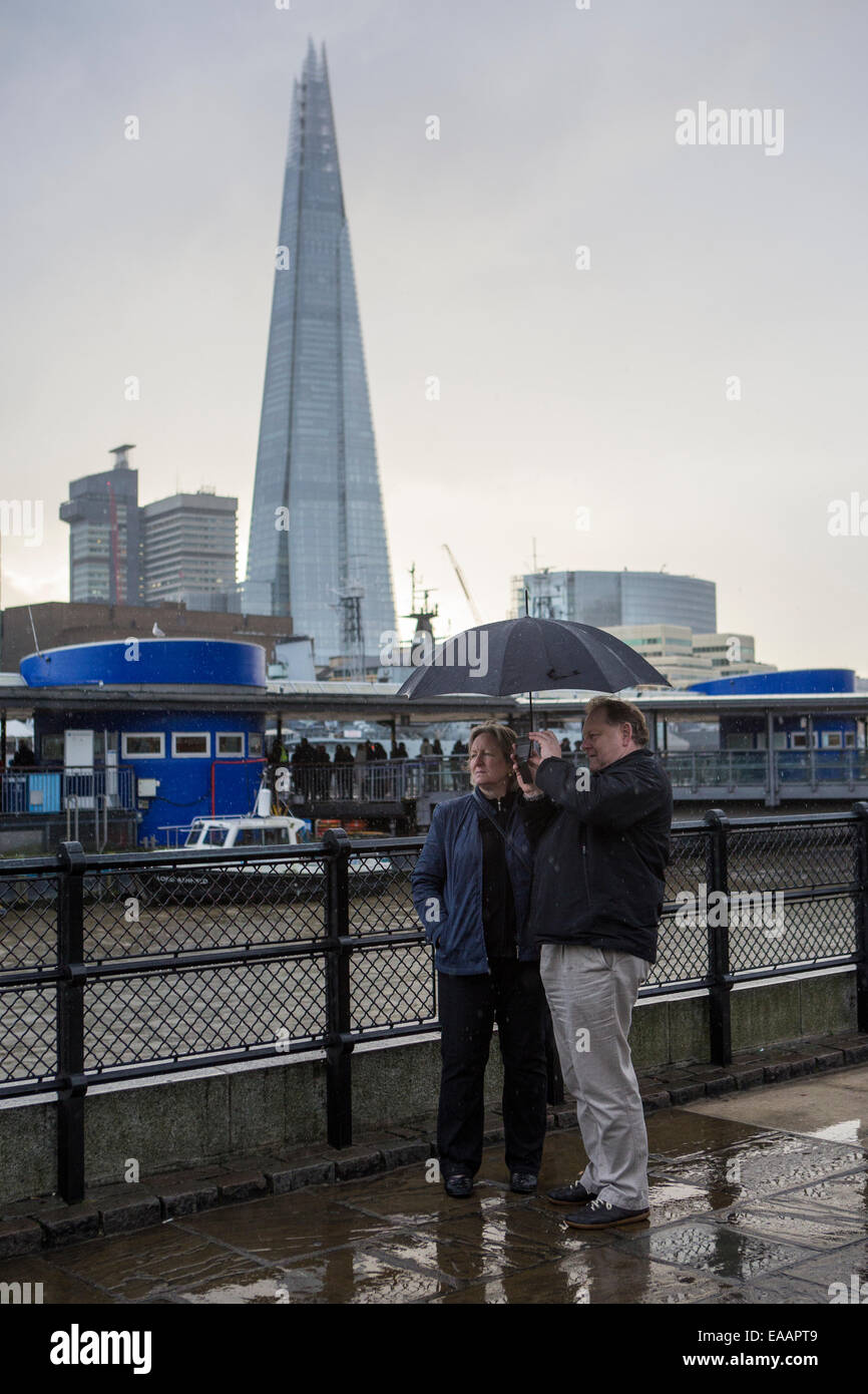 Ein Mann und eine Frau nehmen Sie ein Bild neben der Themse mit dem Shard Gebäude im Hintergrund, während ein Zauberspruch Regen in London Stockfoto