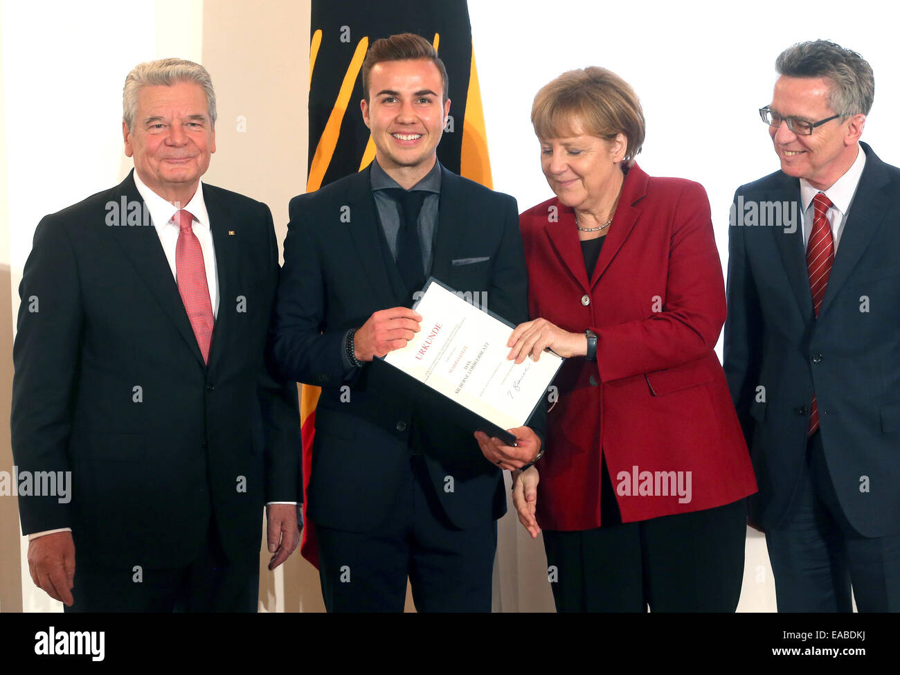 Berlin, Deutschland. 10. November 2014. Deutsche Nationalmannschaft Fußball-Spieler Mario Goetze (2. v. L) zeigt seine Urkunde neben Deutsch Präsident Joachim Gauck (L), die deutsche Bundeskanzlerin Angela Merkel (2. v. R), und deutsche Innenminister Interior Thomas de Maziere (R) in Schloss Bellevue in Berlin, Deutschland, 10. November 2014. Die deutsche Fußball-Nationalmannschaft ist mit dem Award "Silbernes Lorbeerblatt" ausgezeichnet, für den Gewinn der WM 2014 in Brasilien. Foto: WOLFGANG KUMM/Dpa/Alamy Live News Stockfoto