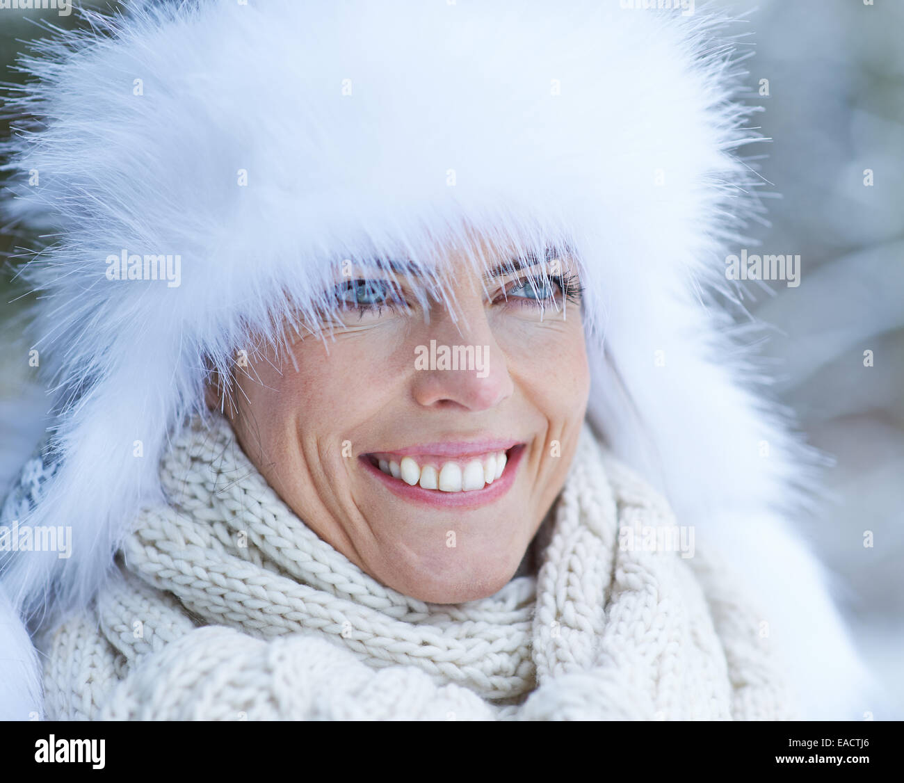 Lächelnde Frau mit weißem Fellmütze im Winterschnee Stockfoto