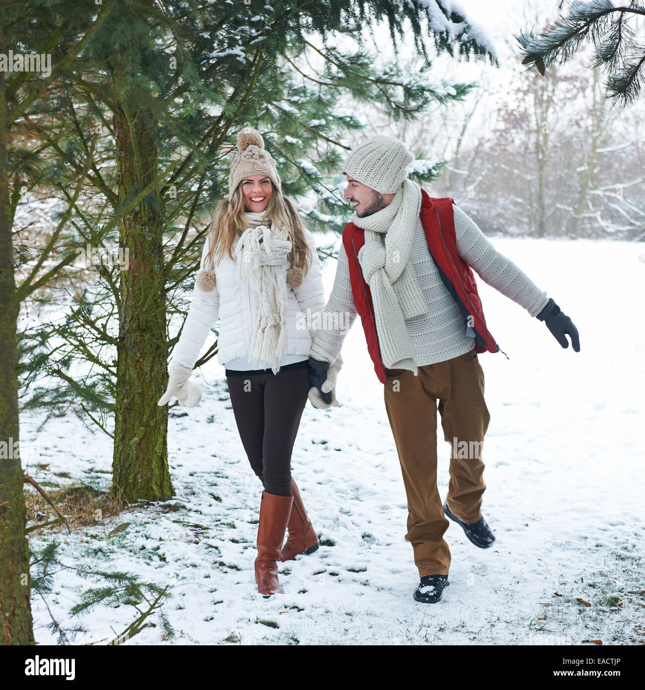 Glücklich lächelnde paar zu Fuß durch den Schnee im Winterwald Stockfoto