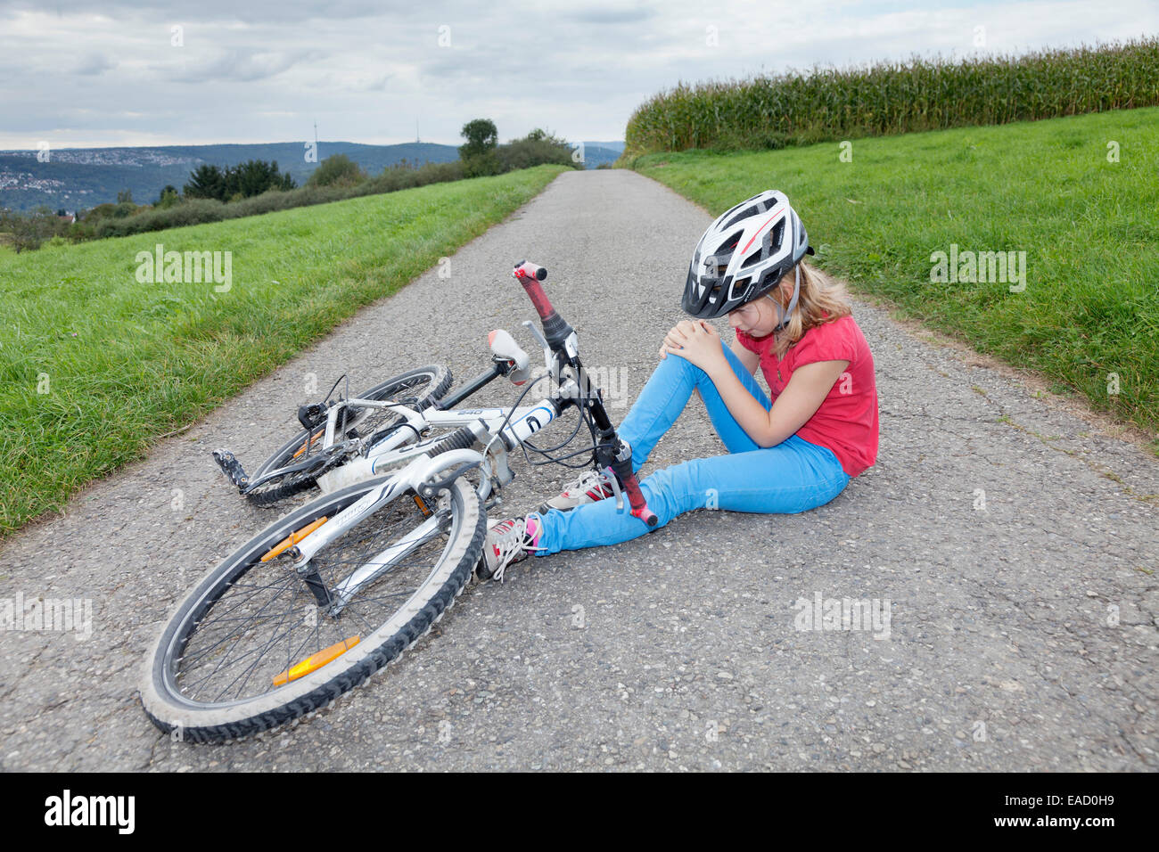 Mädchen, 9 Jahre, das Tragen eines Helms beim Radfahren, halten ihr Knie nach einem Sturz mit dem Fahrrad Stockfoto