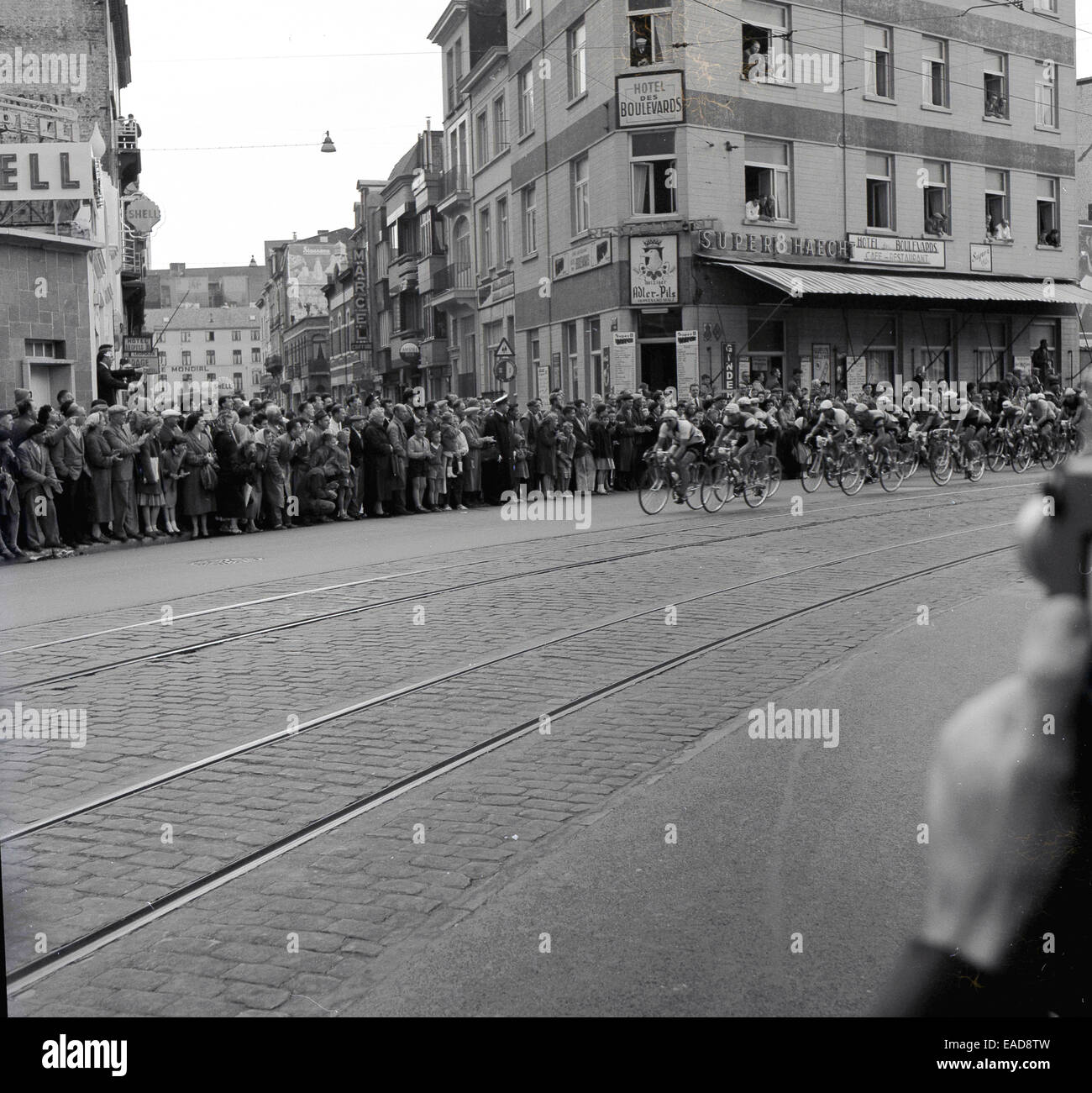 1950er Jahre historische Bild eines Stadtzentrums Radrennen, Belgien mit Fahrern Radfahren über Straßenbahn-Linien auf der Straße. Stockfoto