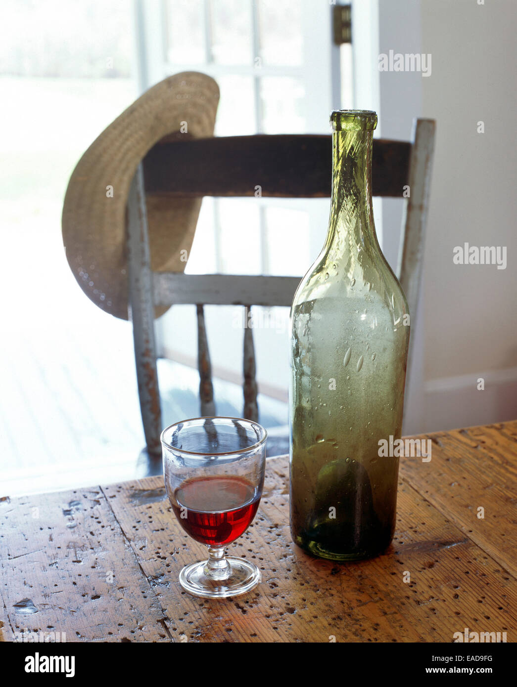 Leere Flasche und Glas Rotwein durch offene Tür mit Strohhut ruht auf Stuhl Stockfoto