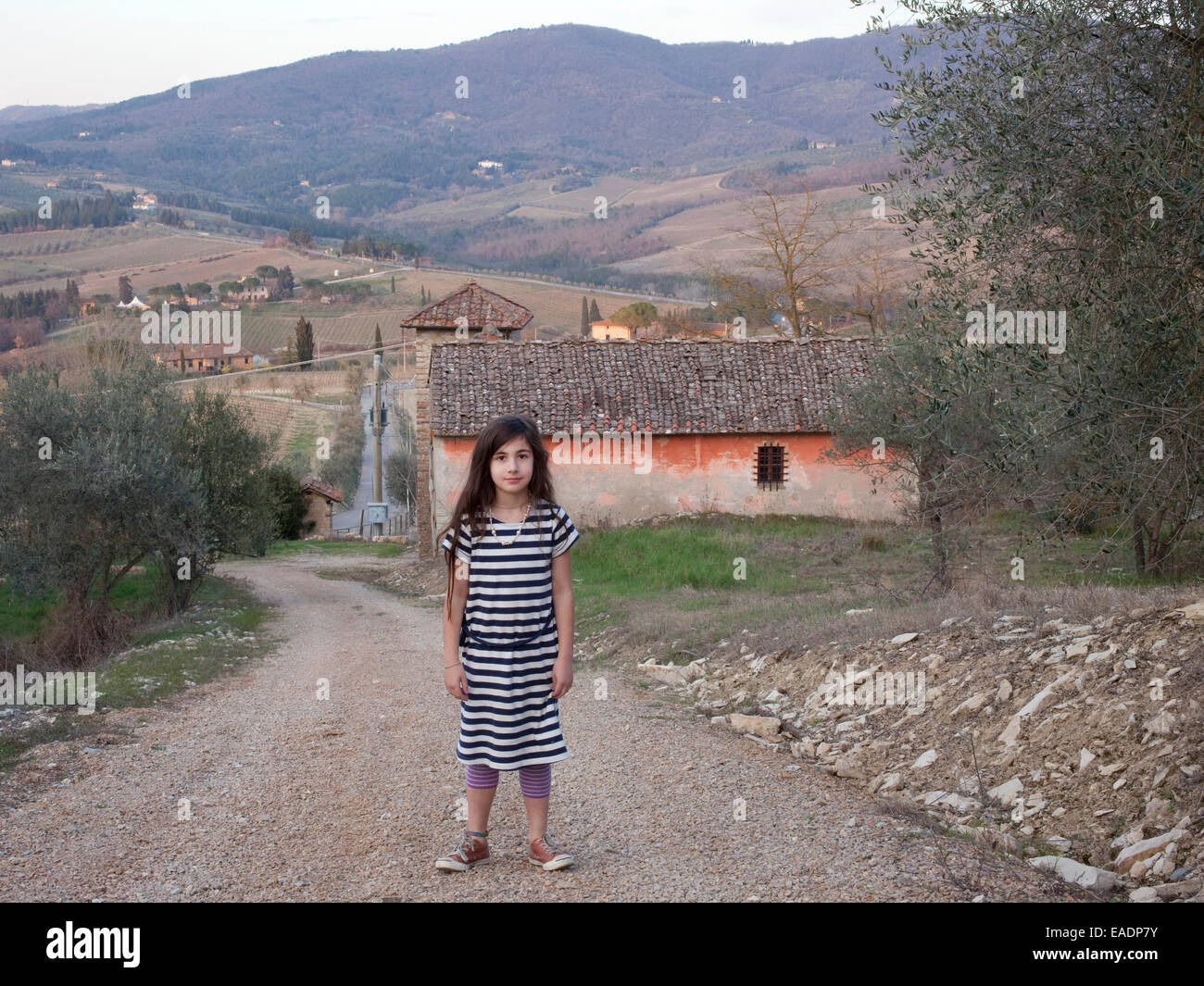 junges Mädchen im gestreiften Kleid steht auf Landstraße in der Toskana, Italien Stockfoto