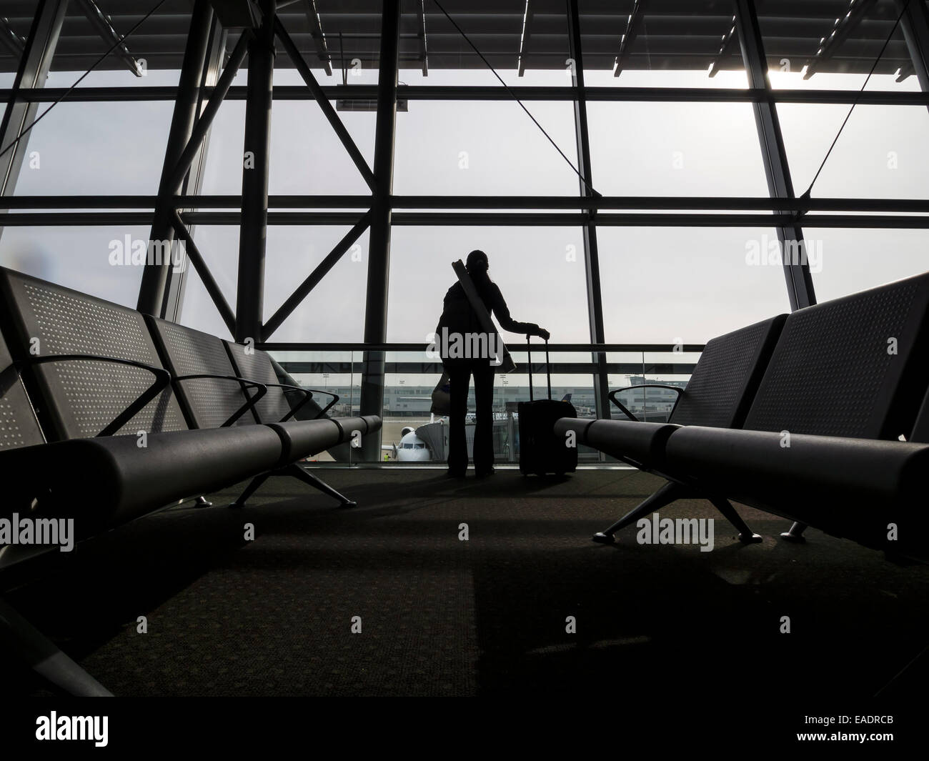 Silhouette einer Person mit einem rollenden Koffer vor einem Flughafen-terminal-Fenster Stockfoto