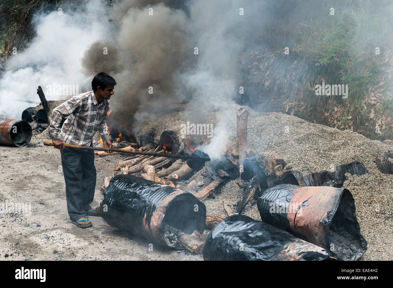 Eine Arbeitskraft, die Mischung aus Kies und heißem Teer auf dem offenen Feuer auf einer Straßenbaustelle, Shimla, Himachal Pradesh, Indien Stockfoto