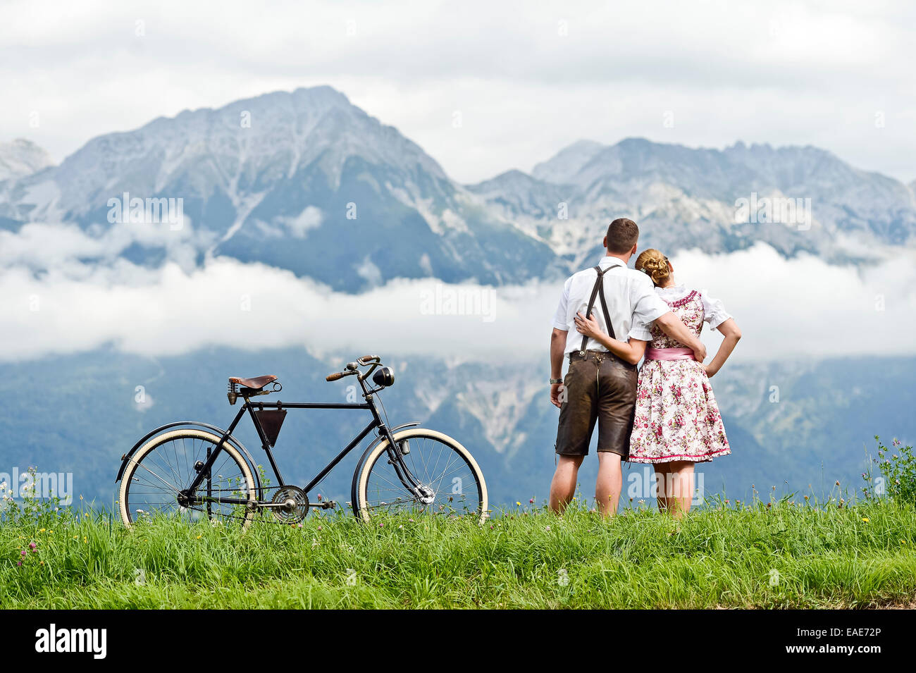 Mann und Frau tragen Tracht mit einem alten Fahrrad mit Blick auf die Berge, Aldrans, Tirol, Österreich Stockfoto