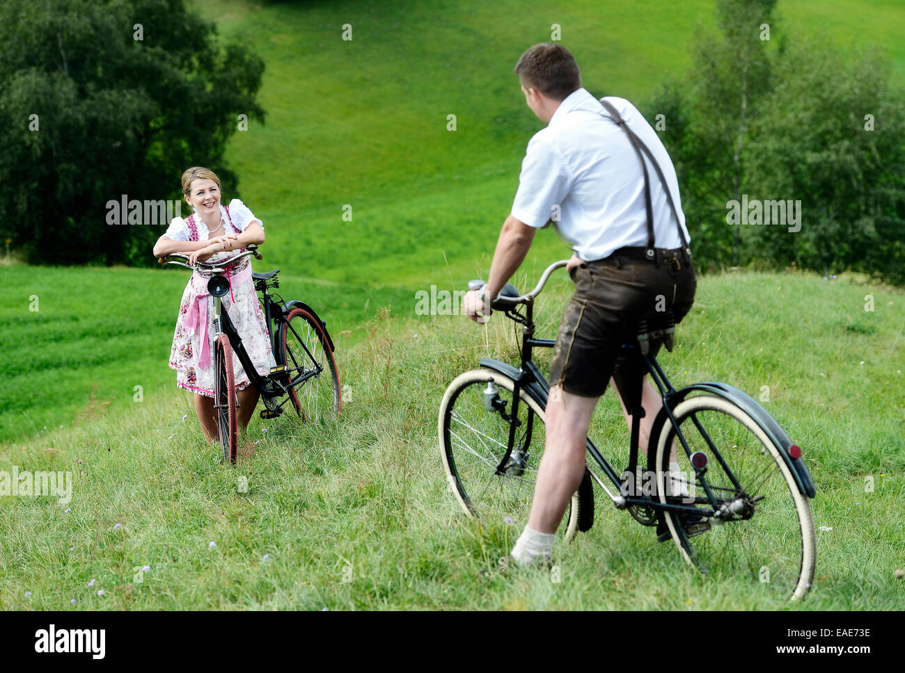 Mann in Lederhose und eine Frau trägt ein Dirndl auf alten Fahrrädern innerhalb einer natürlichen Landschaft, Igls, Innsbruck, Tyrol Stockfoto