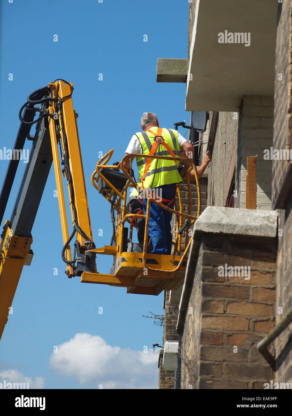 Handwerker-Zement zeigen die Außenseite eines Gebäudes auf einer Hubarbeitsbühne Fahrzeug bequem näher an das Dach gehievt. Stockfoto