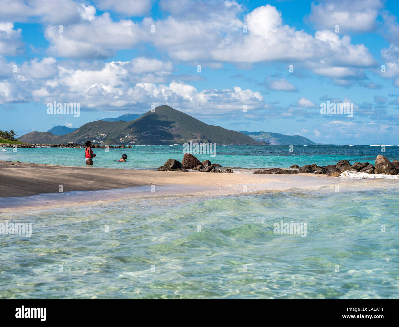 Karibische Seascape, exotischen Strand Long Haul Bay, Nevis mit paar Baden im blauen Meer, St Kitts im Hintergrund. Stockfoto