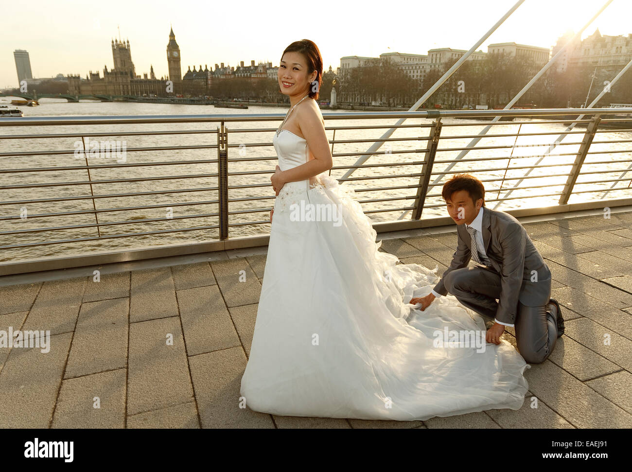 Eine asiatische Braut hat ihr Hochzeitskleid angeordnet nach ihrem Bräutigam vor Stadtbild von London und Westminster - Hintergrundbeleuchtung durch Sonne Stockfoto