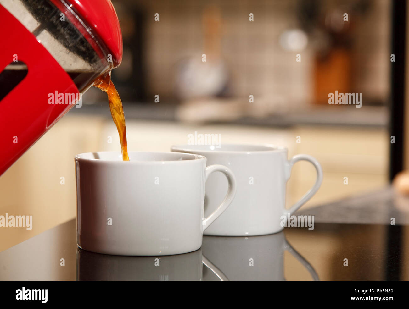Gemahlenen Kaffee gegossen aus einem roten Getränketablett in zwei weiße Tassen Stockfoto