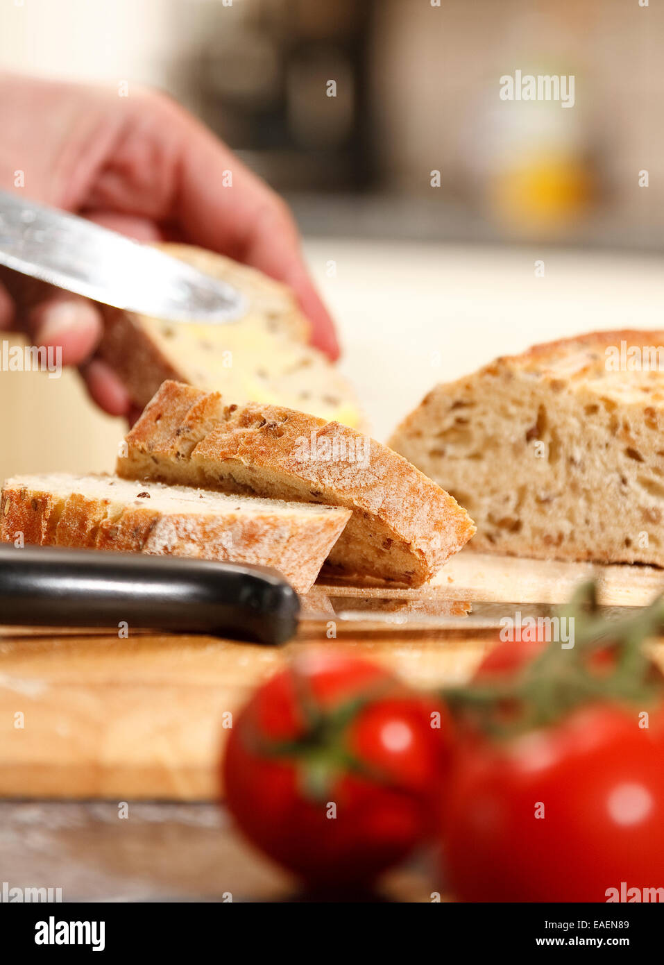 Kernigen Roggen Brot in einer heimischen Küche - Mann verbreiten Slice, Fokus auf restlichen Scheiben Stockfoto