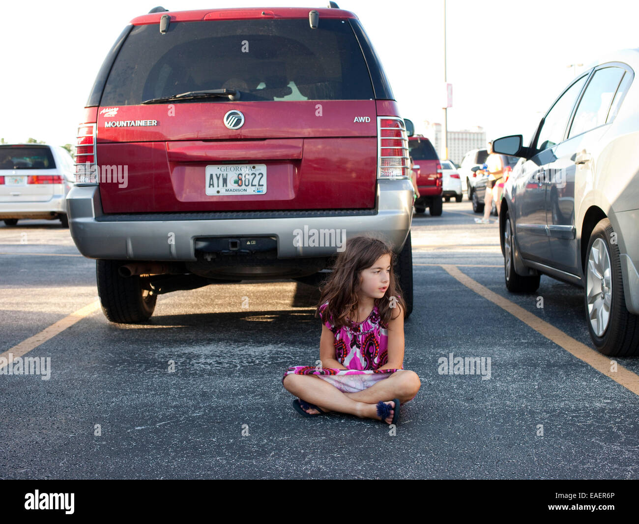 Ein junges Mädchen in einem bunten Kleid sitzt auf einem Parkplatz und wartet Stockfoto