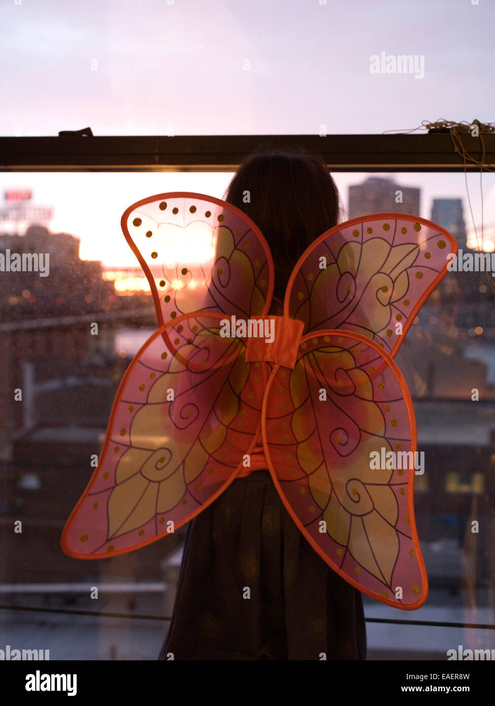 junges Mädchen mit Schmetterlingsflügeln Stadt Fenster Blick bei Sonnenuntergang Stockfoto