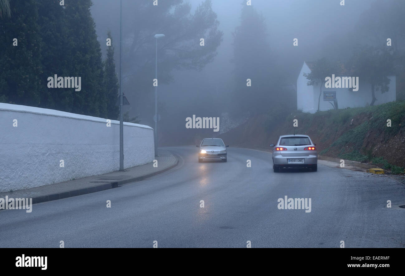 Zwei Autos fahren im Nebel. Ein Auto mit einem Scheinwerfer nicht funktioniert. neblige Bergstraße. Spanien. Stockfoto