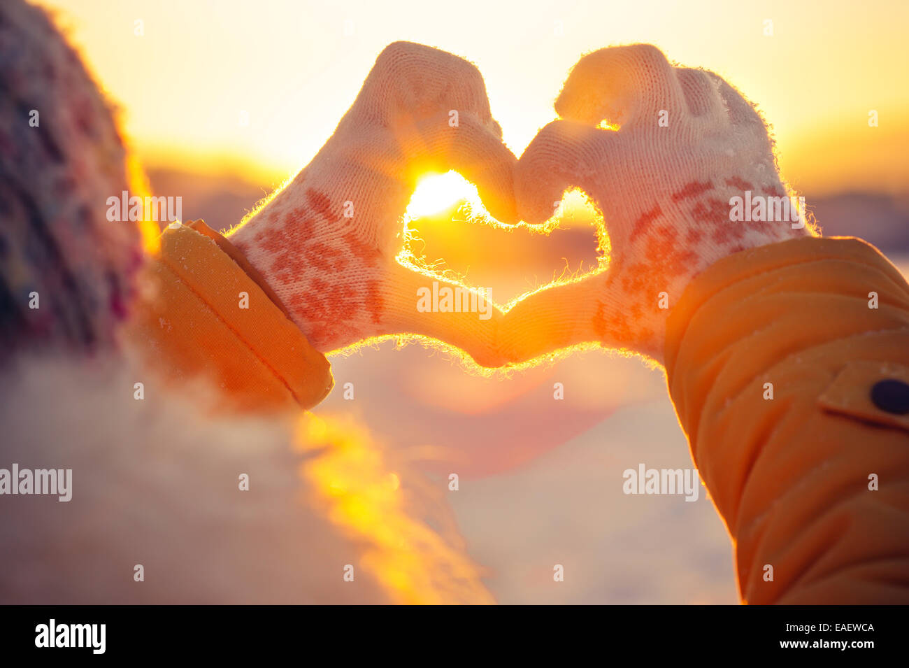 Frau Hände im Winterhandschuhe Herzsymbol Lifestyle und Gefühle Konzept mit Sonnenuntergang-Licht-Natur auf Hintergrund geprägt Stockfoto