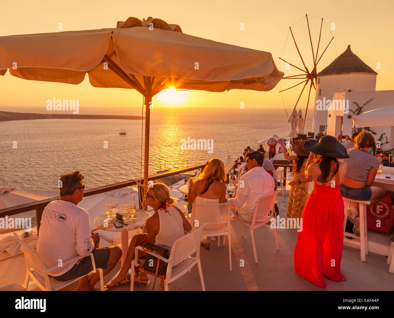 Überfüllten Bar und Windmühle bei Sonnenuntergang durch die Ägäis, Oia, Santorini (Thira) Kykladen, griechische Inseln, Griechenland, Europa Stockfoto