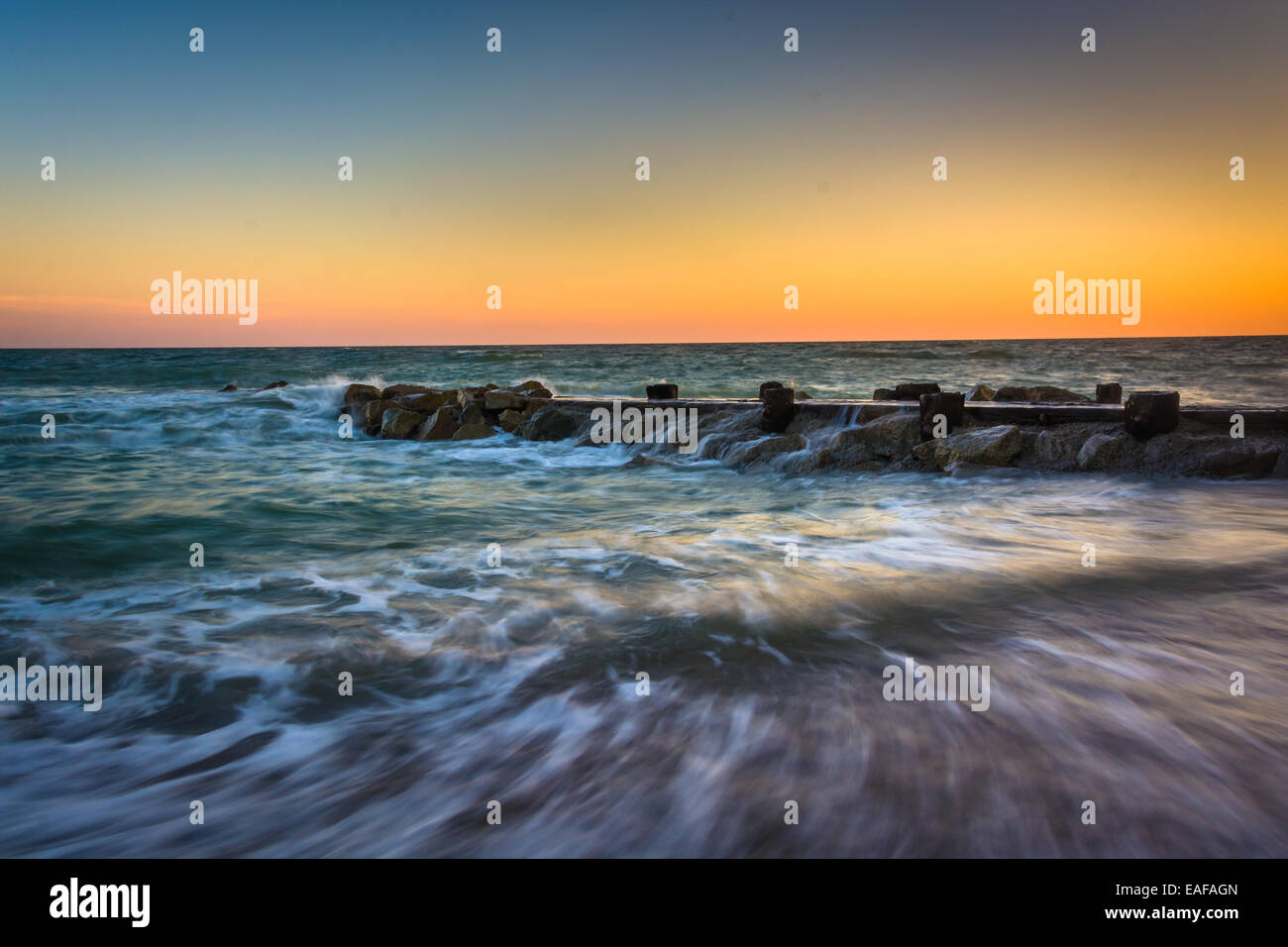 Wellen und eine Mole bei Sonnenuntergang im Atlantischen Ozean bei Edisto Beach, South Carolina. Stockfoto