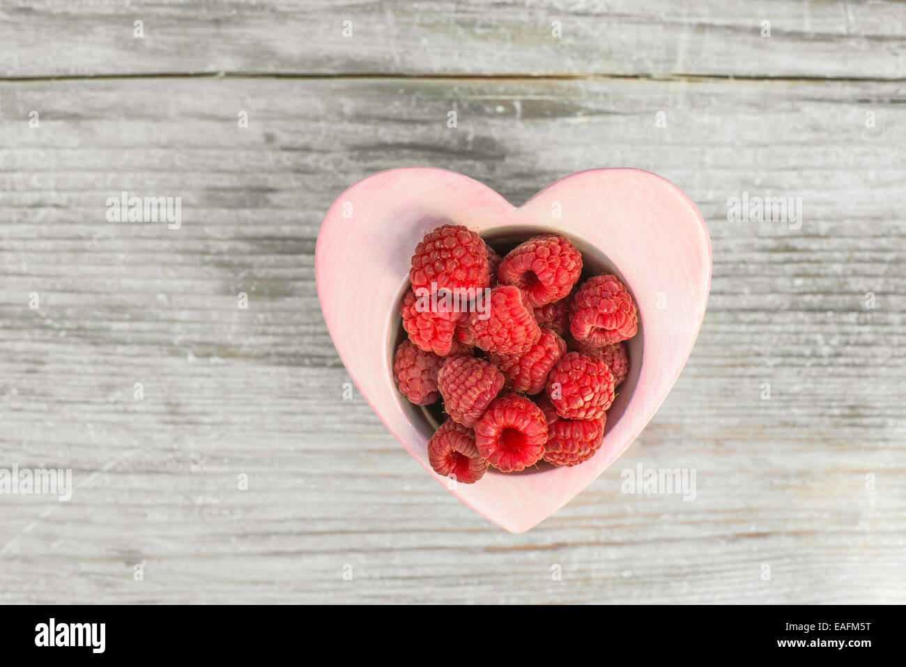 Himbeeren in eine Schüssel auf Holz. Herz-Form-Schüssel. Stockfoto