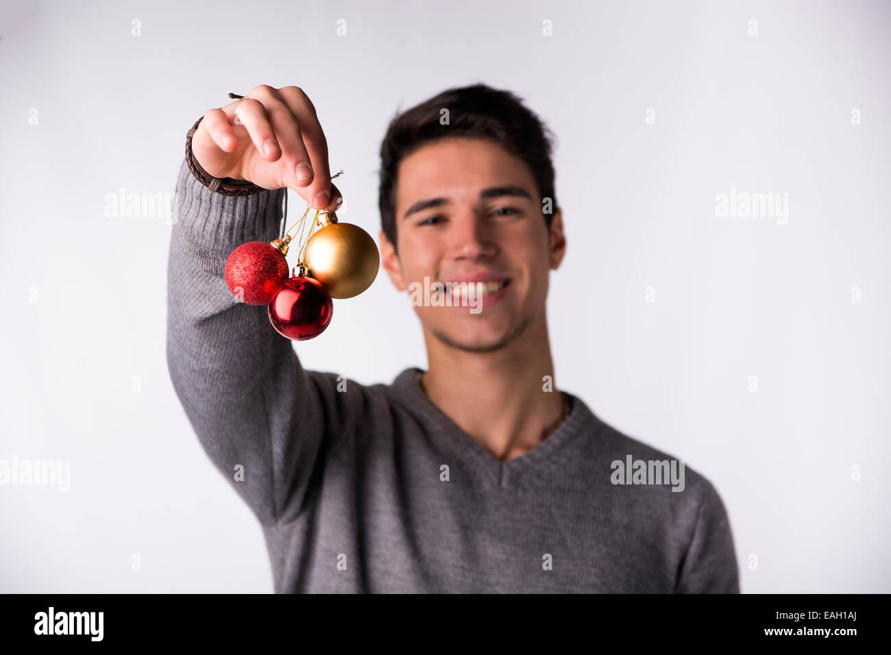 Hübscher junger Mann lächelnde und Holding Christbaumkugeln vor seinem Gesicht, Blick in die Kamera auf weißem Hintergrund Stockfoto