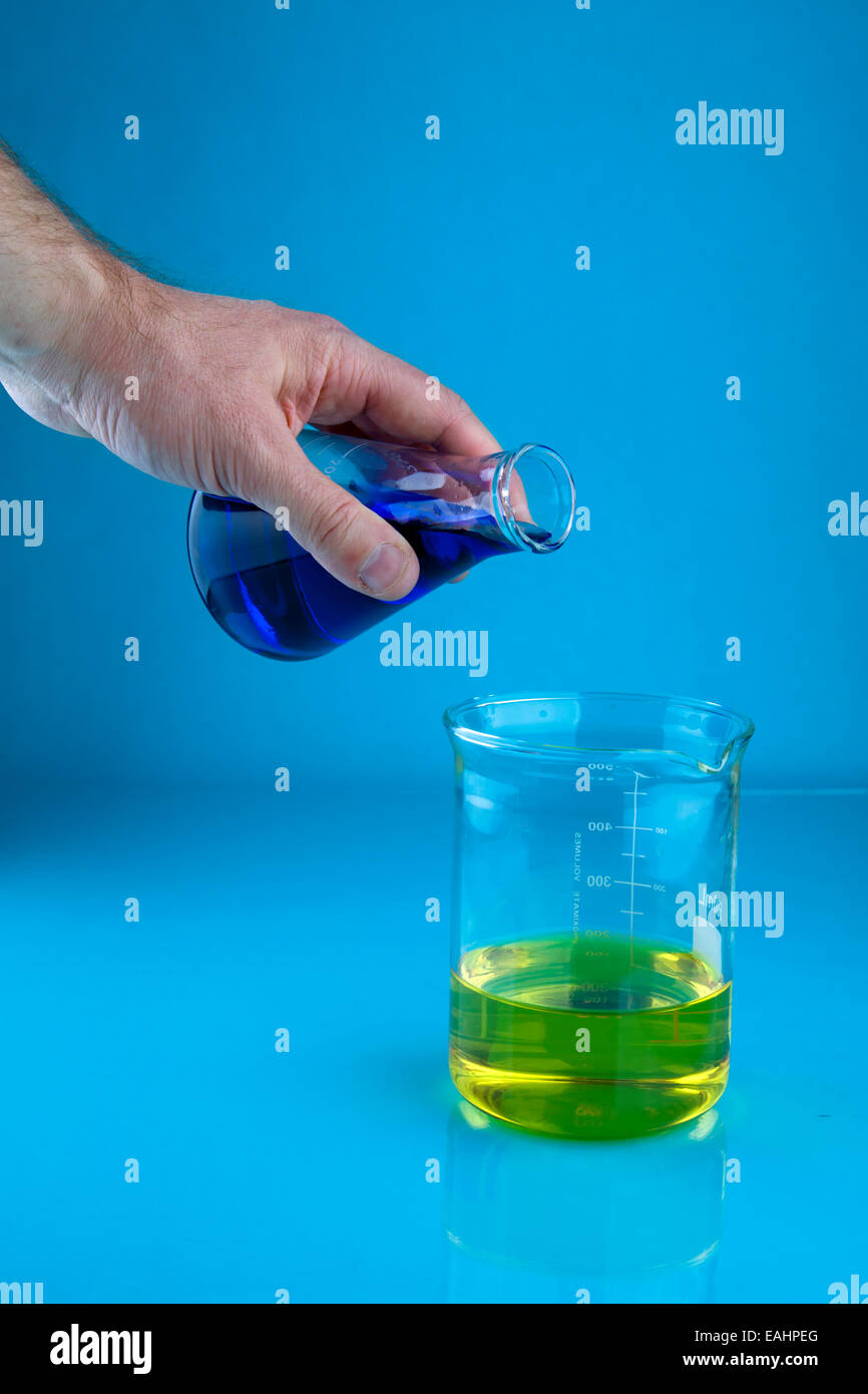 Eine blaue Flüssigkeit Gießen in einen Becher mit einer gelben Flüssigkeit, so dass eine grüne Flüssigkeit Stockfoto