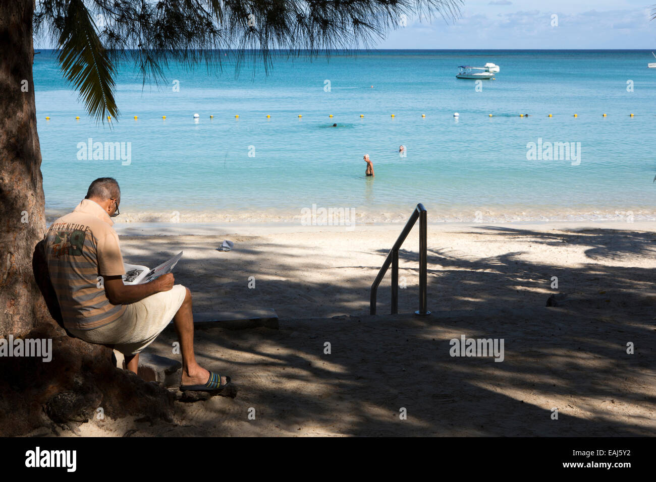 Mauritius, Pereybere, öffentlichen, Strand, Mann sitzend, liest Zeitung im Schatten Stockfoto