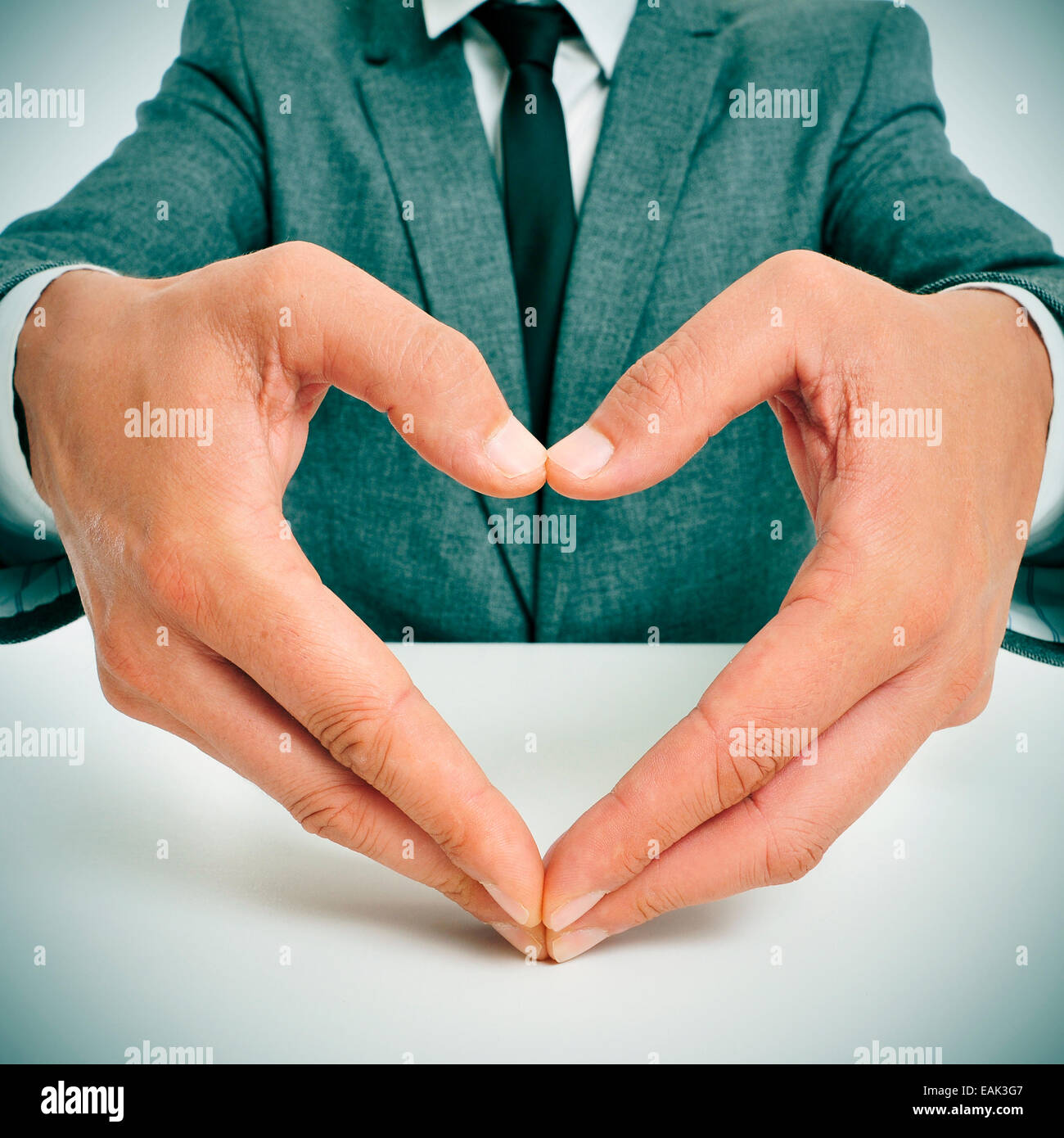 Mann in einem Anzug sitzt in einer Tabelle bilden ein Herz mit seinen Händen Stockfoto